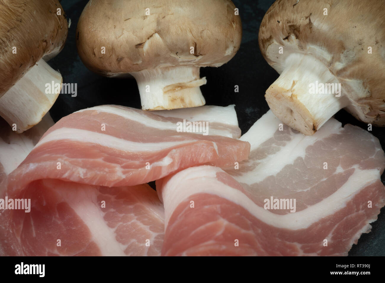 Close up materie dry-cured back bacon e funghi su una pietra scura piatto Foto Stock