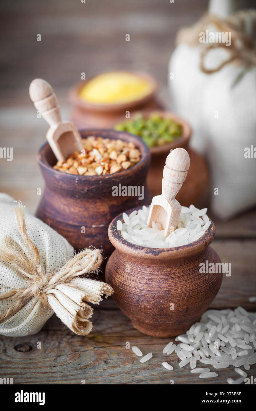 Creta rustica vasi riempiti con riso, verde mung, mais, grano saraceno e sacchi di grano sul background. Foto Stock