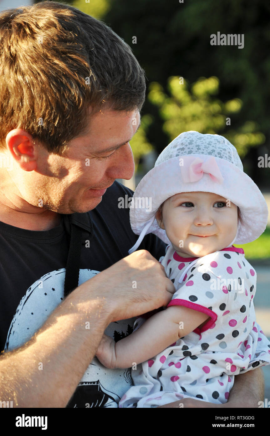 Carino sorridente bambina in un cappello nelle braccia di suo padre a piedi nella soleggiata giornata estiva. Foto Stock