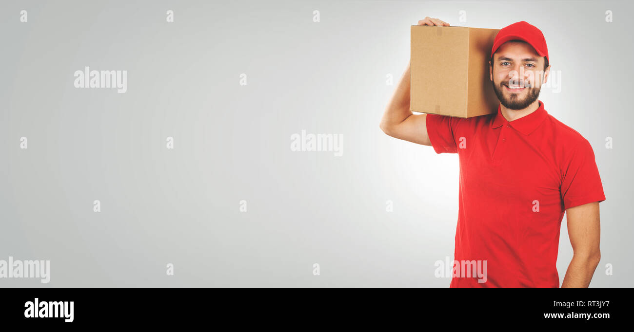 Giovani consegna sorridente uomo in rosso uniforme e con scatola di spedizione sulla spalla. spazio copia Foto Stock