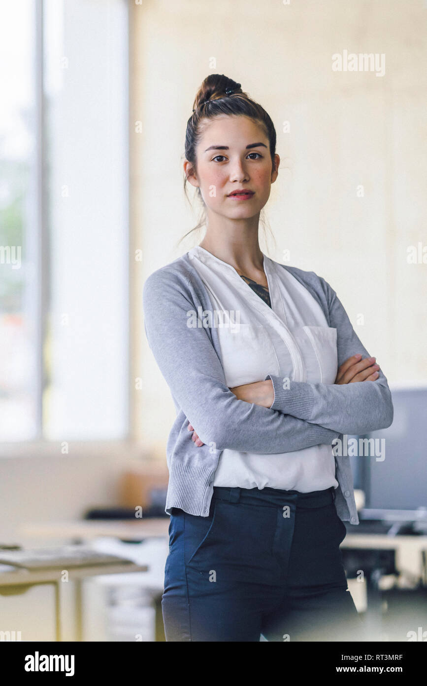 Ritratto di una giovane e bella donna in piedi in ufficio con le braccia incrociate Foto Stock