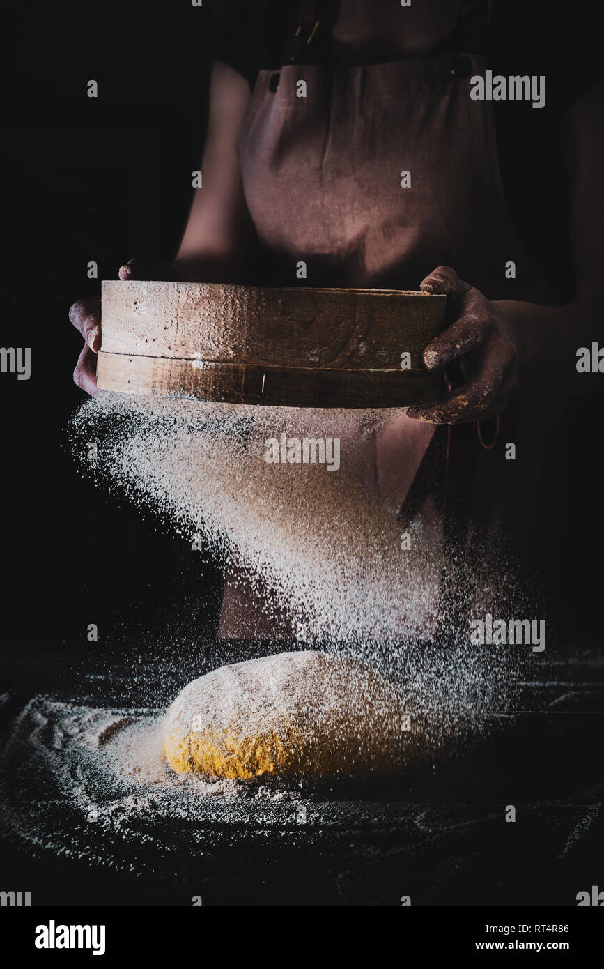 Donna setacciare la farina attraverso un setaccio per la produzione di pane, scuro moody immagine creativa Foto Stock