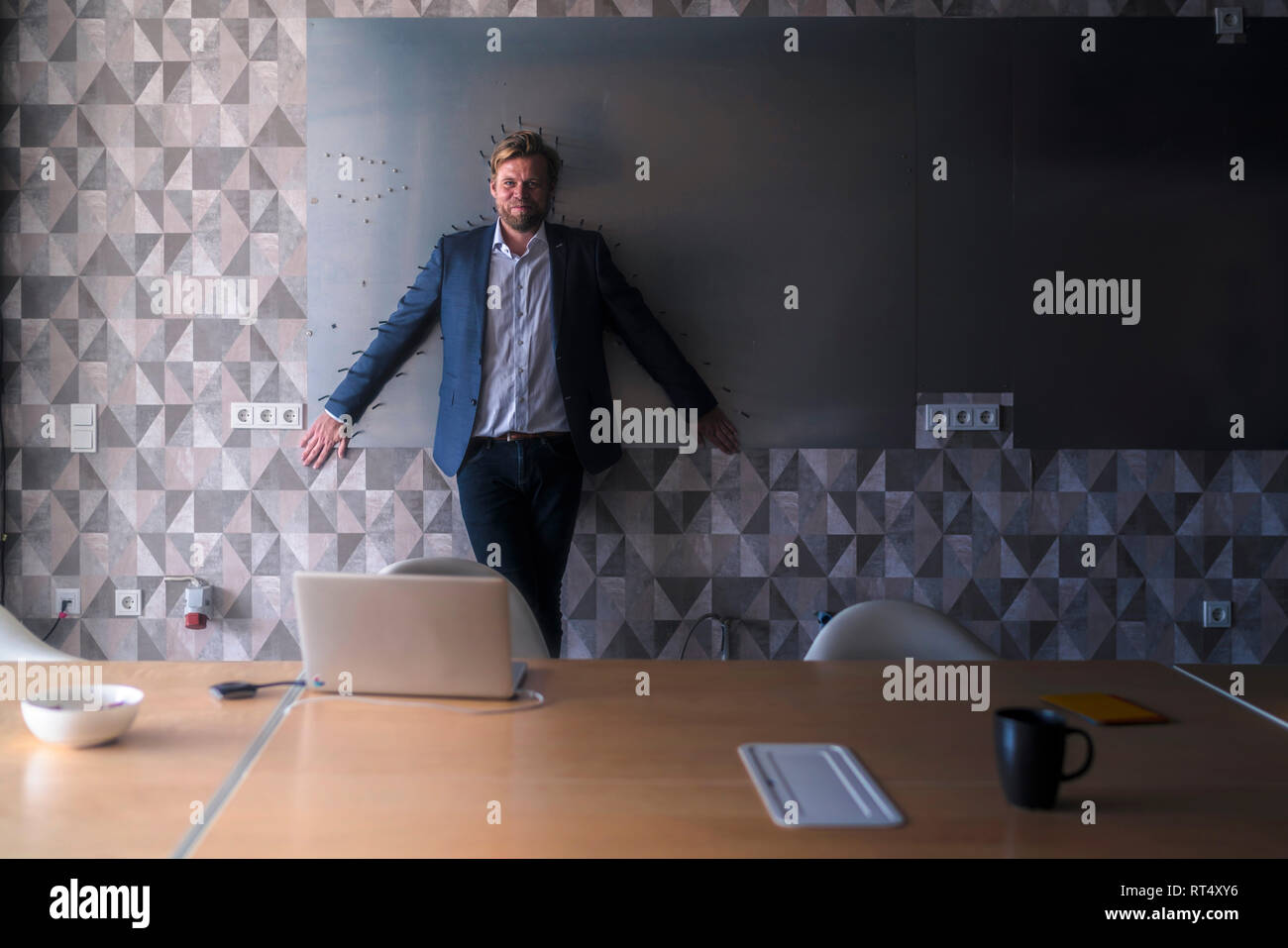 Imprenditore standiing nella sala riunioni con il dorso di un magnete a parete, incorniciato dalle frecce Foto Stock