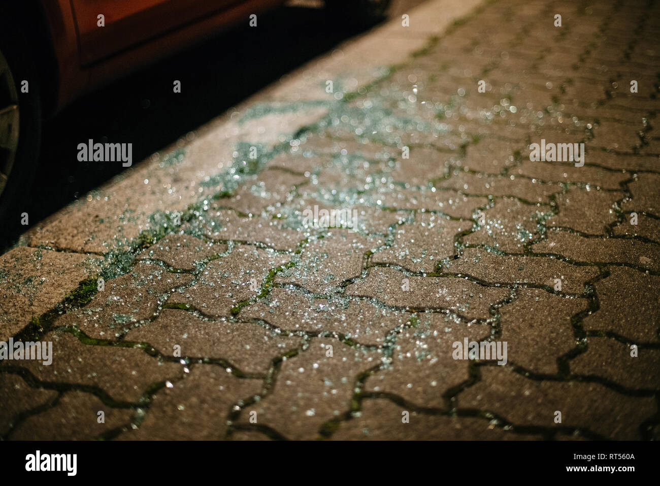 Vetro frantumato in miriadi di pezzi si vede sulla strada vicino alla macchina parcheggiata di notte - ladro di tracce o di incidente Foto Stock