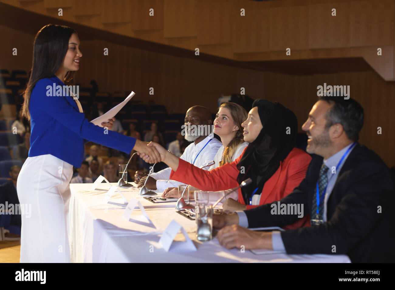 Business donna agitando la mano per il collega di lavoro in auditorium Foto Stock