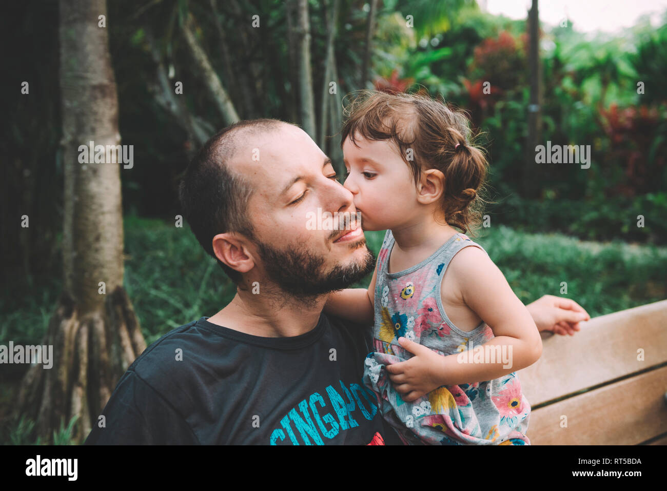 Baby ragazza baciare suo padre sulla guancia in un parco Foto Stock