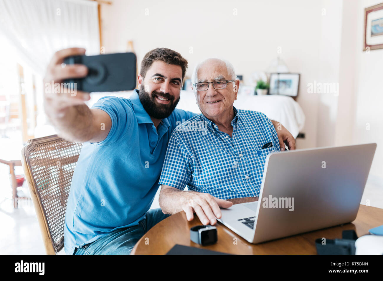 Ritratto di adulto nipote e suo nonno tenendo selfie con lo smartphone a casa Foto Stock