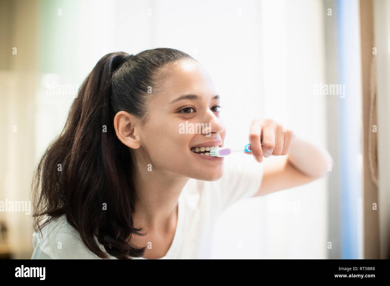 Donna felice spazzolare i denti in Specchio bagno Foto Stock