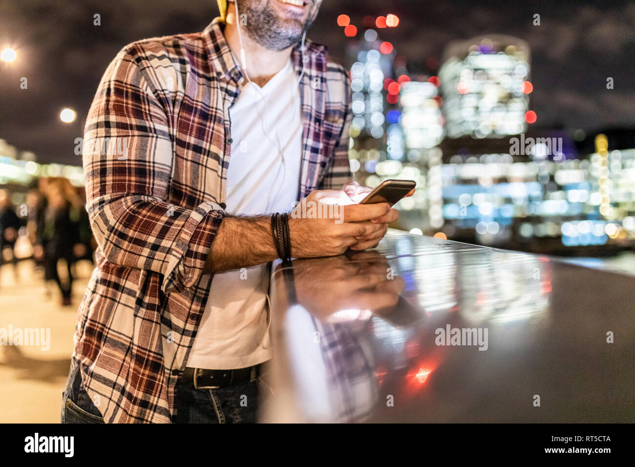 UK, Londra, close-up di uomo appoggiato su di una ringhiera con un telefono cellulare con le luci della città in background Foto Stock