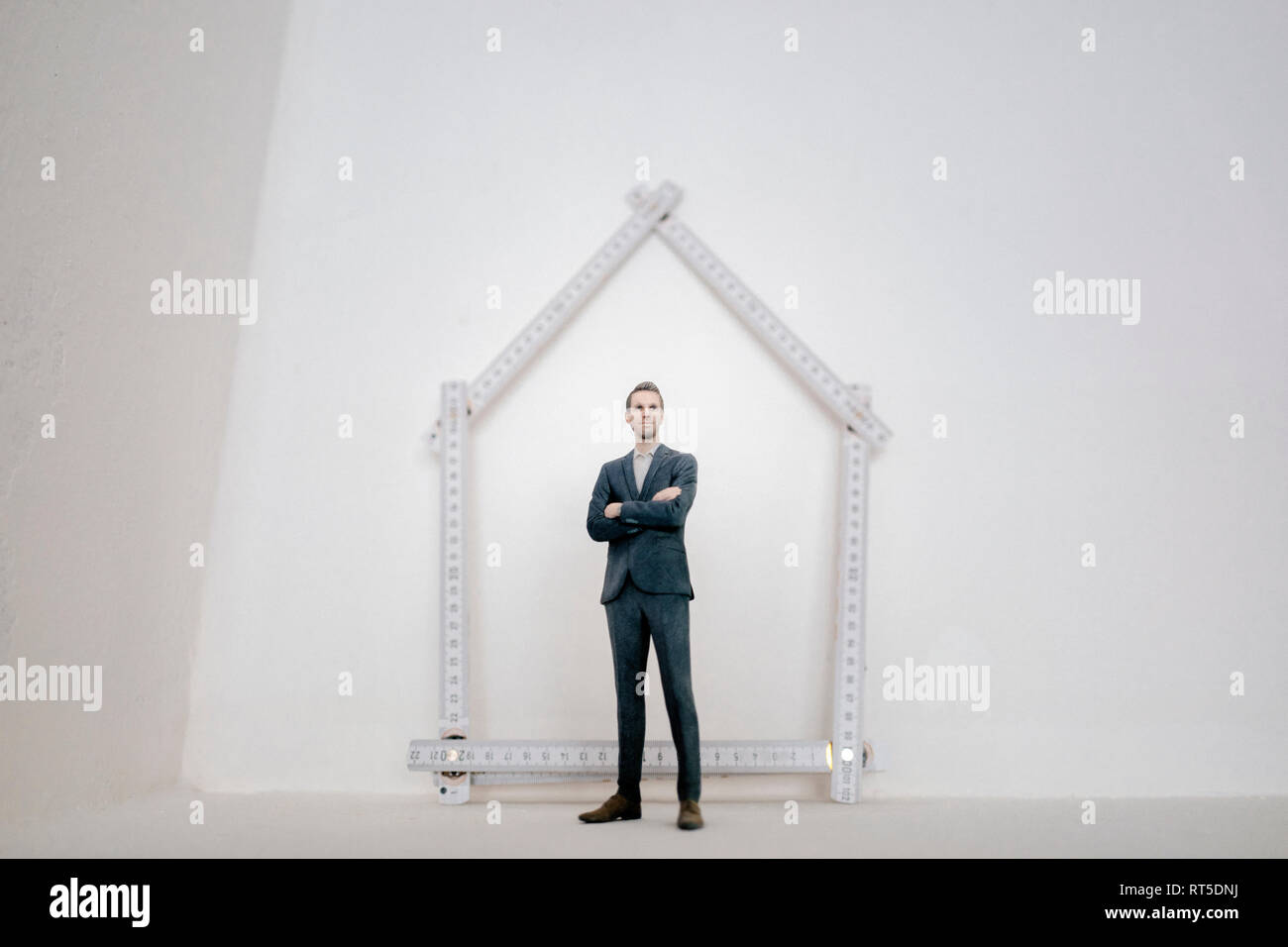 Imprenditore figurina in piedi sulla tavola con pocket regola, sagomando una casa Foto Stock