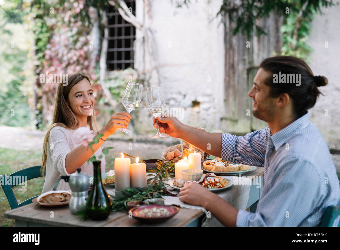Coppia avente un romantico pasto candelight accanto a un cottage tintinnanti bicchieri di vino Foto Stock