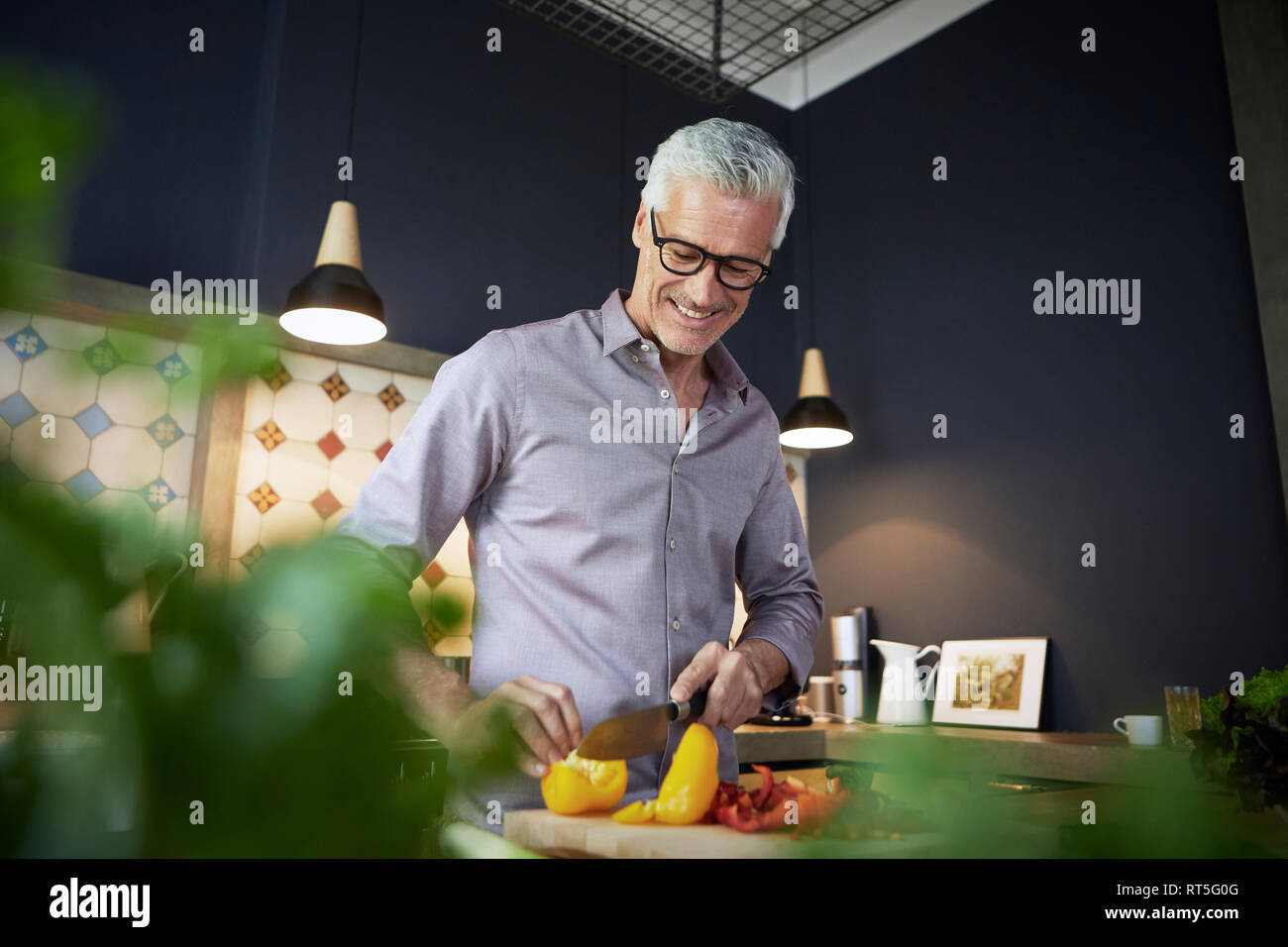 Sorridente uomo maturo tritare il peperone in cucina Foto Stock