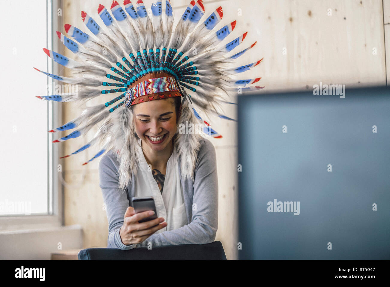 Giovane donna indossare copricapo indiano, stando in ufficio, smartphone usinag Foto Stock