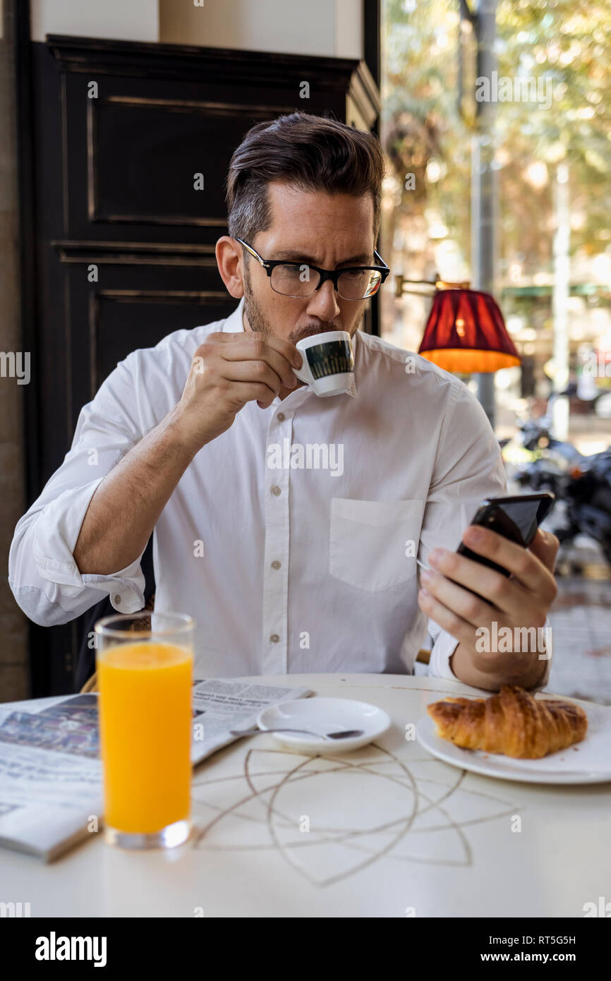 Imprenditore avere la prima colazione in un caffè e un controllo del telefono cellulare Foto Stock