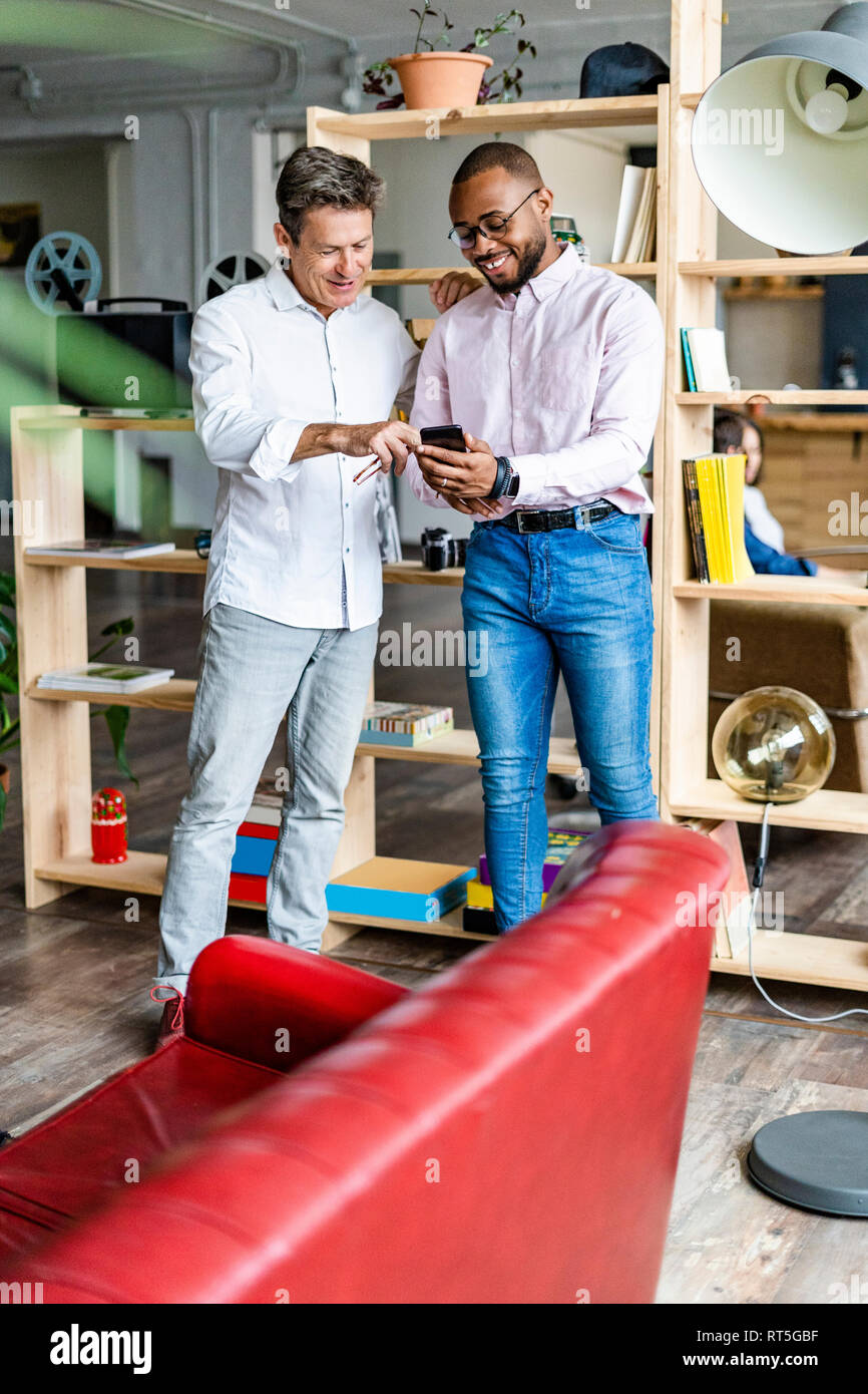 Due imprenditori sorridente utilizzando il cellulare in ufficio loft Foto Stock