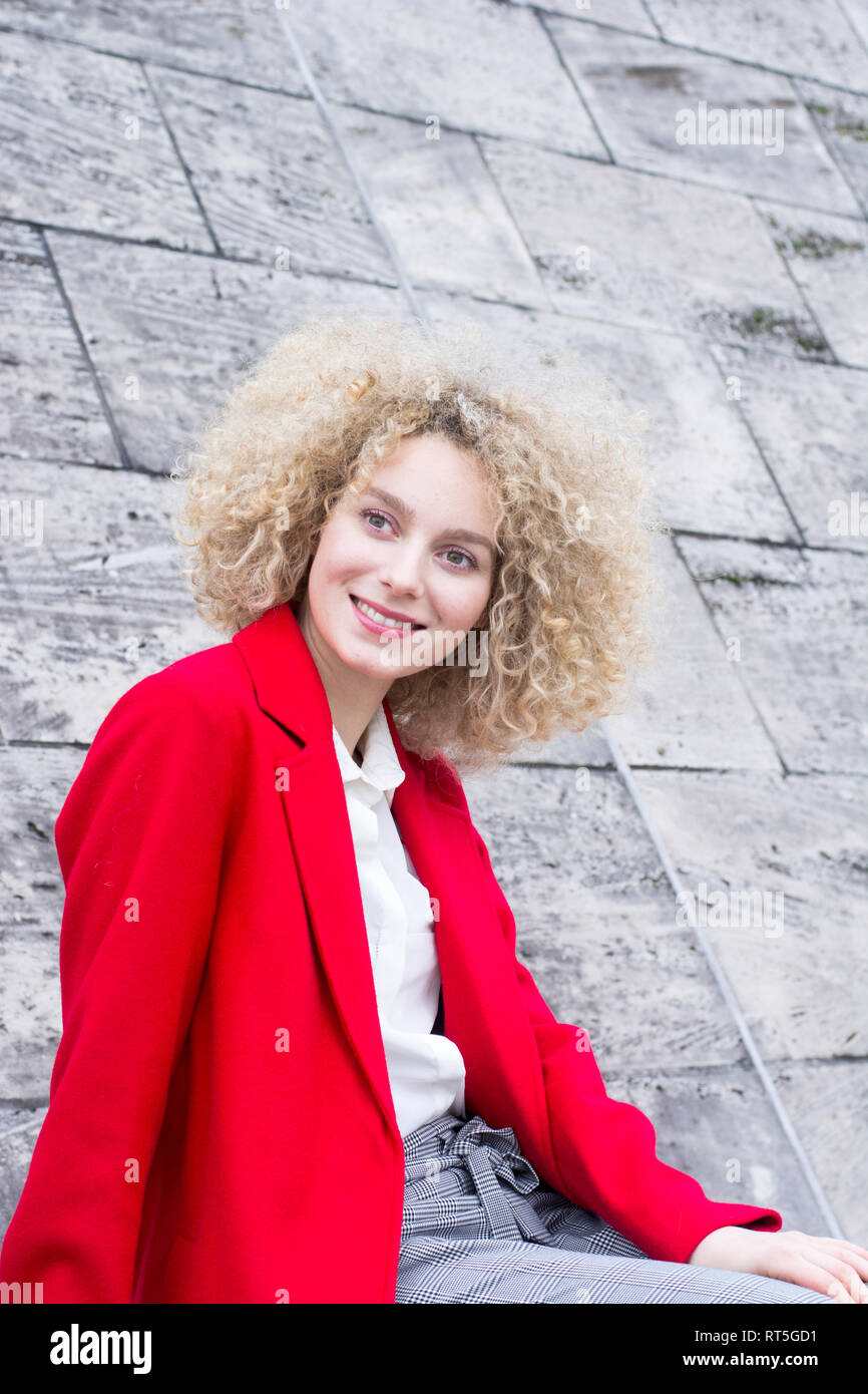 Ritratto di sorridere donna bionda con boccoli indossando cappotto rosso Foto Stock