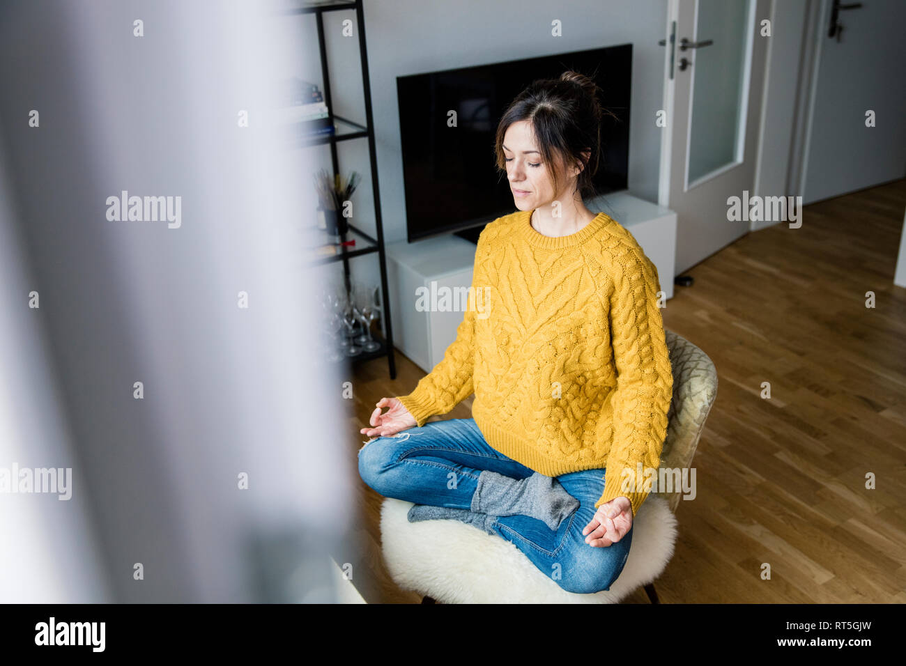 Coppia donna seduta con le gambe incrociate sulla sedia con gli occhi chiusi, meditando a casa Foto Stock