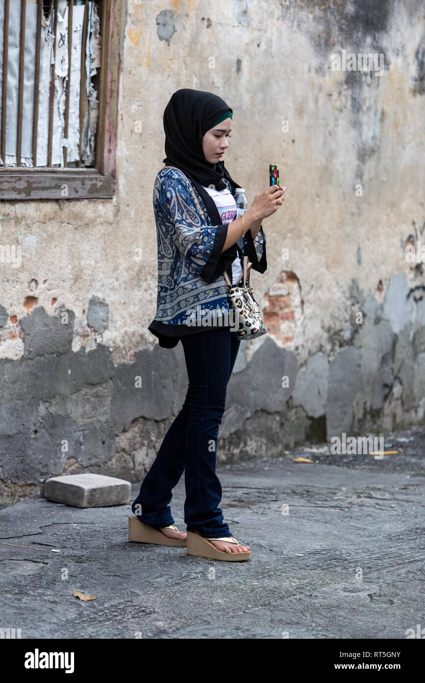 George Town, Penang, Malaysia. Giovane donna malese di scattare una foto con il suo telefono cellulare. Foto Stock