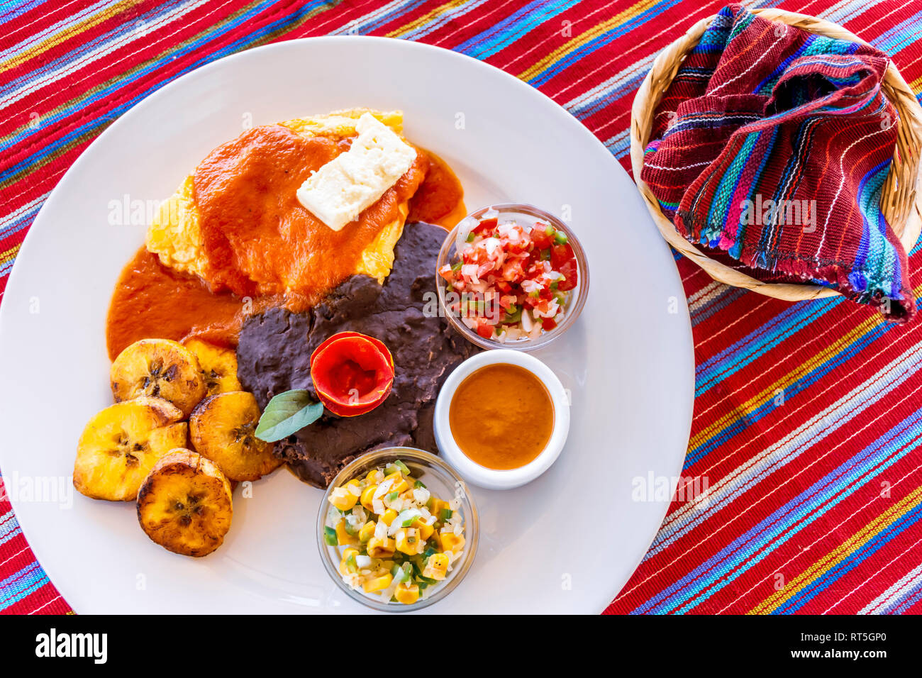 Tradizionale colazione guatemalteco di uova, fagioli neri, formaggio & plantano fritte con tortillas avvolto in cesto su intrecciato Maya tovaglia tessili. Foto Stock