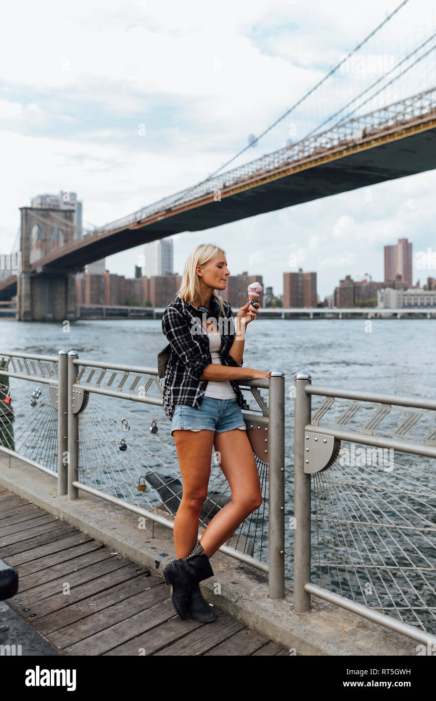 Stati Uniti d'America, la città di New York, Brooklyn, giovane donna in piedi di fronte al porto di mangiare un gelato Foto Stock