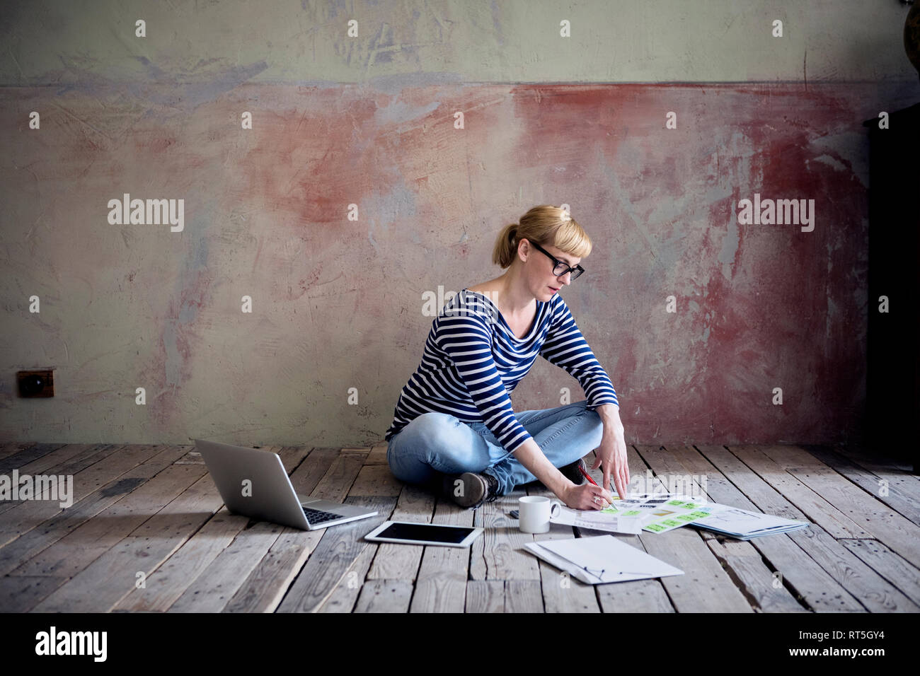 Donna seduta su pavimento di legno in una camera non rinnovate di un loft a lavorare Foto Stock