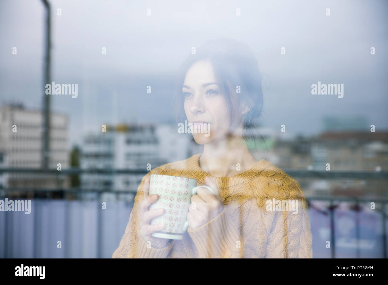 Triste donna in piedi presso la finestra, bere il tè Foto Stock