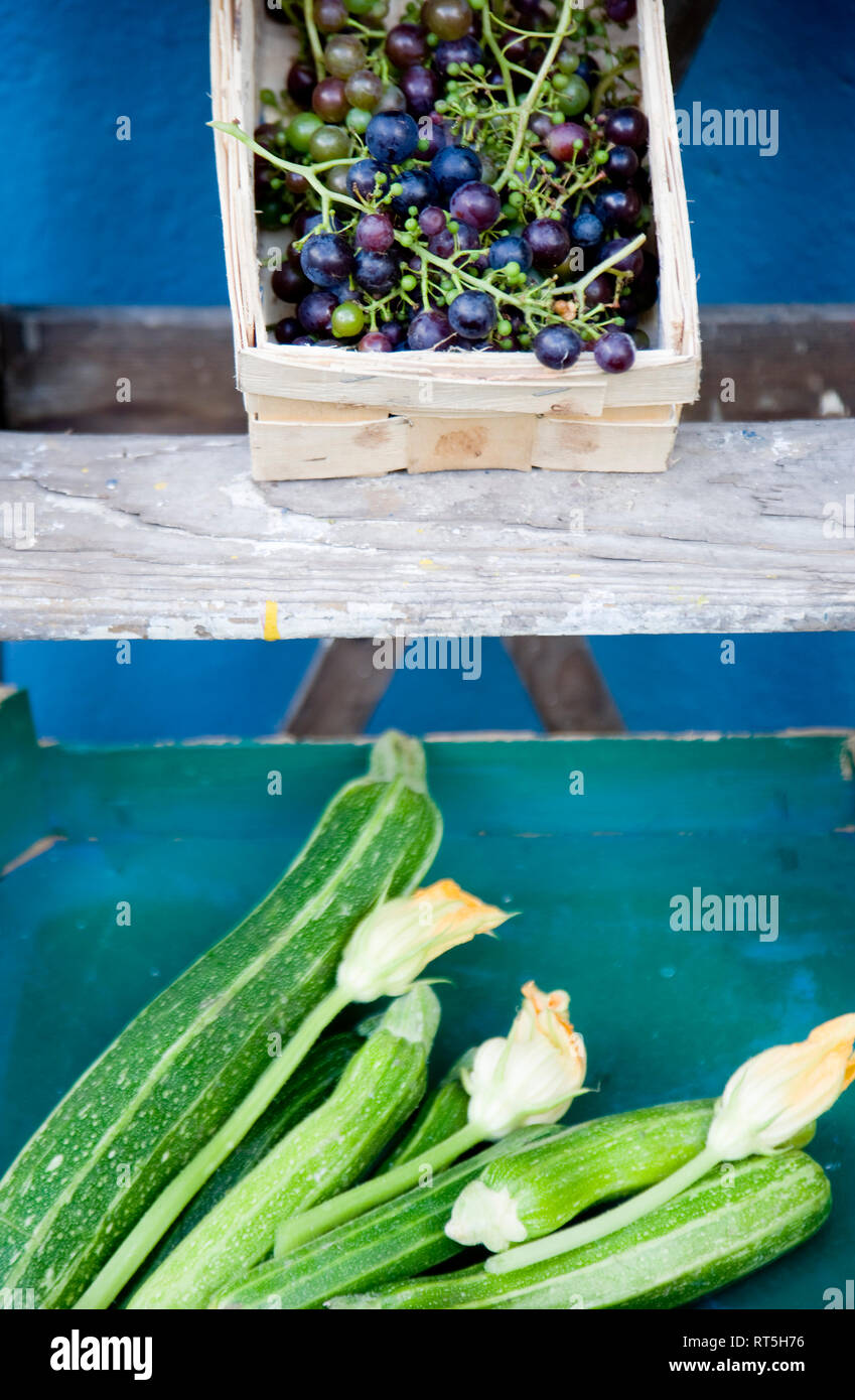 Scaletta, cesto con uve blu, box con zucchine e fiori Foto Stock