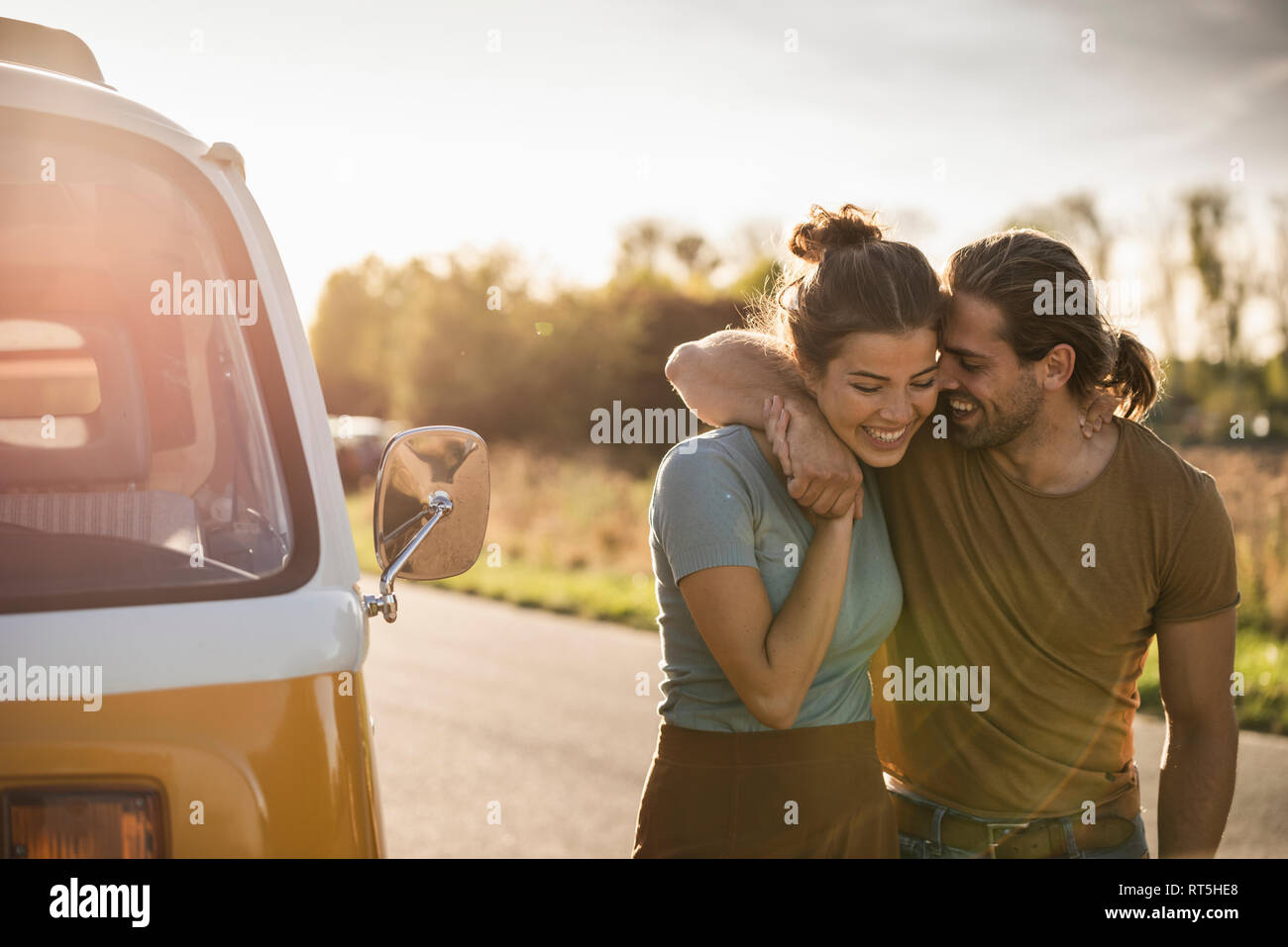 Affettuosa giovane di camminare sulla strada con bracci intorno, accanto al loro camper Foto Stock