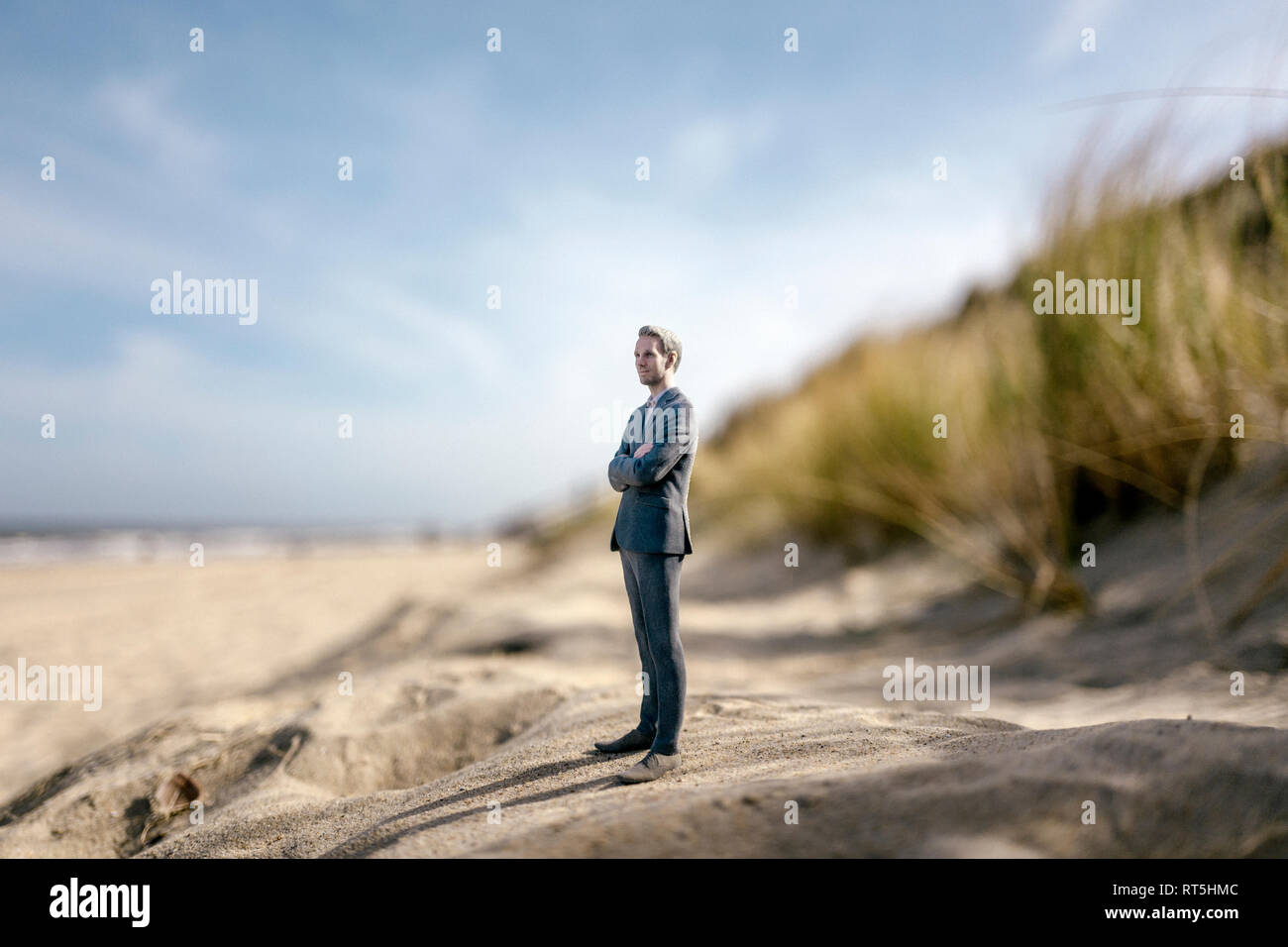 Imprenditore figurina permanente sulla duna di sabbia, guardando a distanza Foto Stock