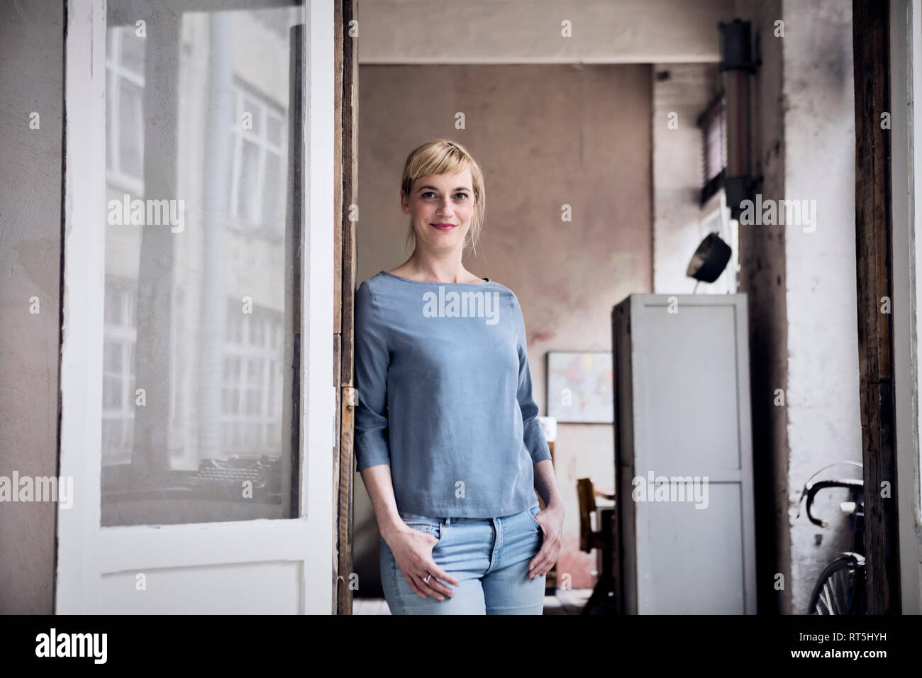 Ritratto di donna sorridente appoggiato contro il telaio della porta in un loft Foto Stock