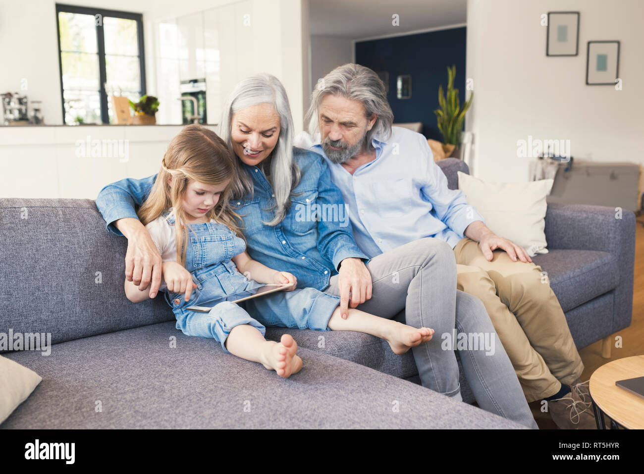 Nonni e nipote seduta sul lettino, utilizzando tablet Foto Stock