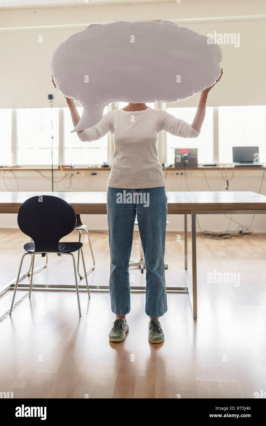 Donna in piedi in ufficio, tenendo gonfiabile di fumetto discorso davanti al suo volto Foto Stock