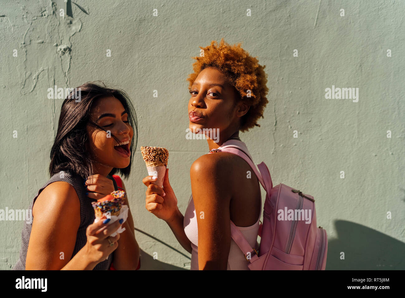 Due happy amici di sesso femminile con coni gelato che pongono a una parete Foto Stock