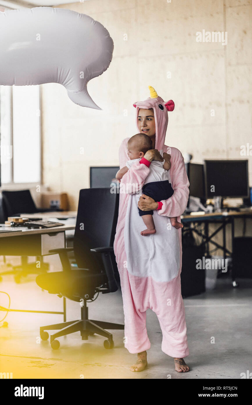 Giovane madre in unicorn onesie, tenendo il suo figlio nelle sue braccia con il discorso di bolla sopra la sua testa Foto Stock