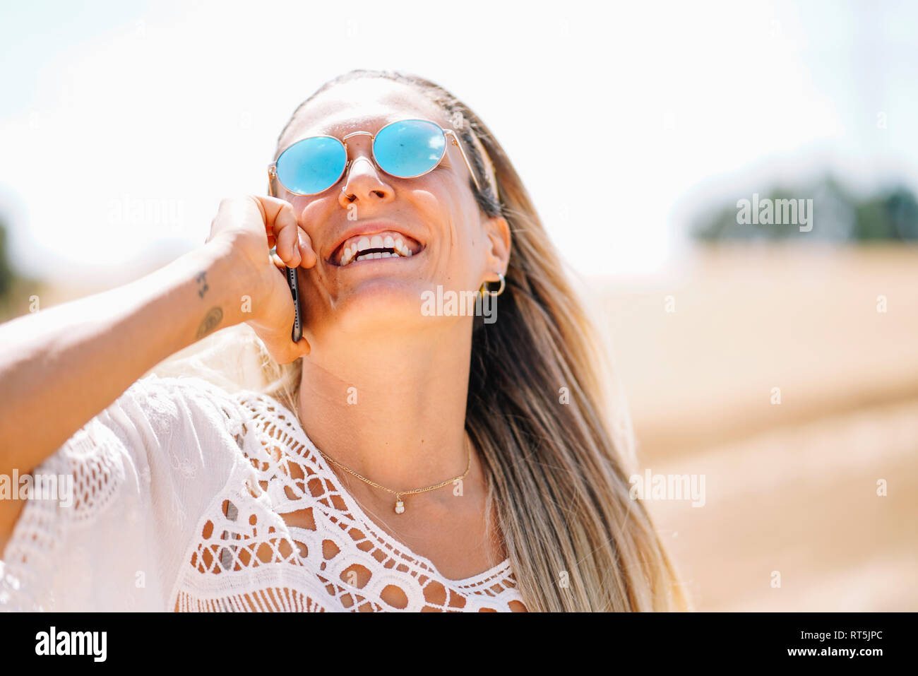 Ridere ragazza bionda al telefono indossando occhiali da sole con mirroring Foto Stock