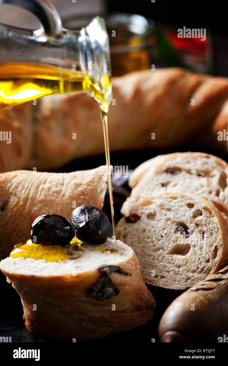 Versando l'olio d'oliva sulla fetta di pane ad anello con olive nere Foto Stock