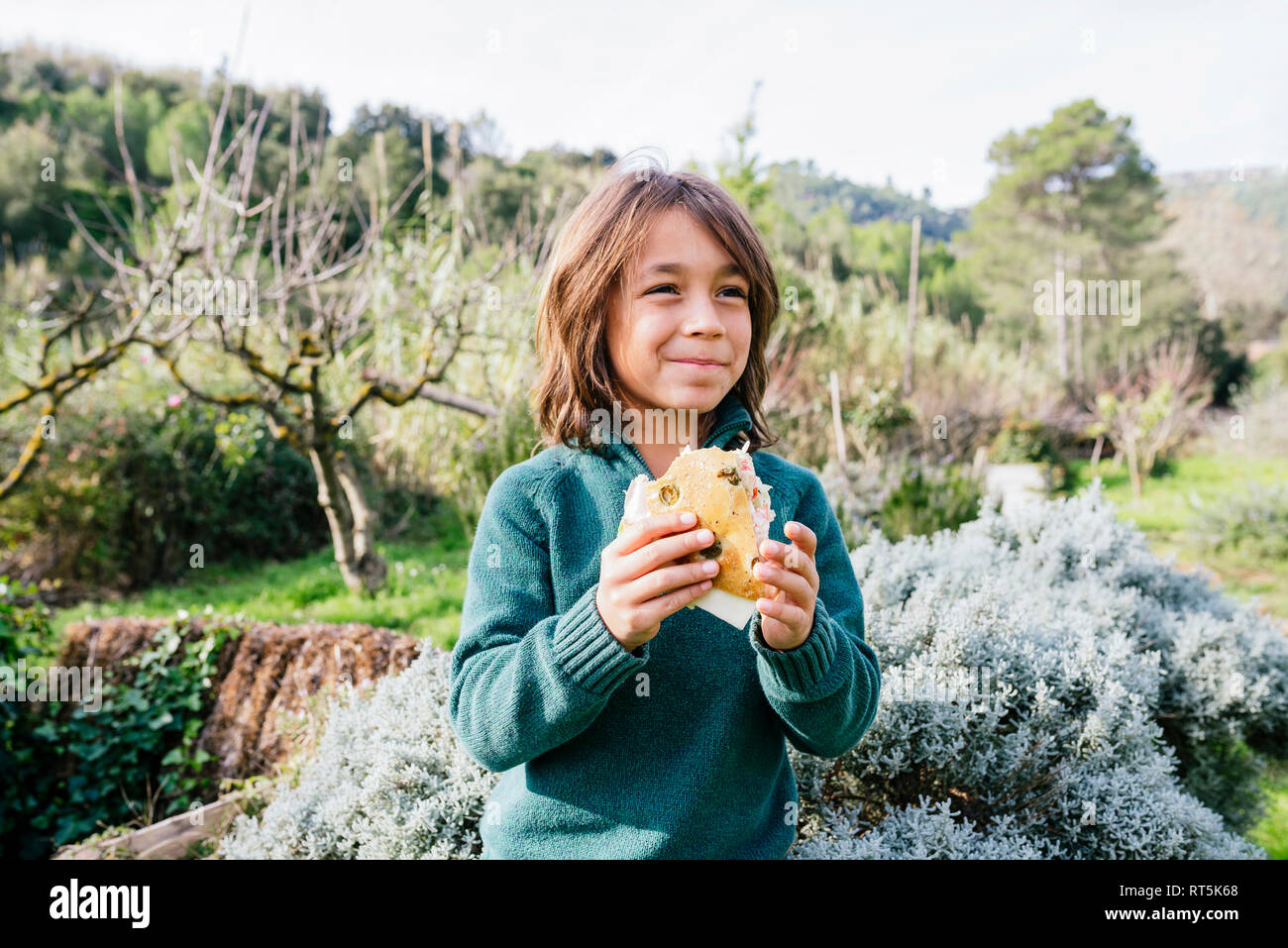 Ragazzo in piedi in giardino, prendendo una pausa, mangiando panini Foto Stock