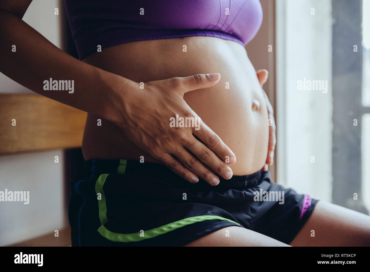 Sportivo da donna incinta mentre tiene il suo ventre Foto Stock