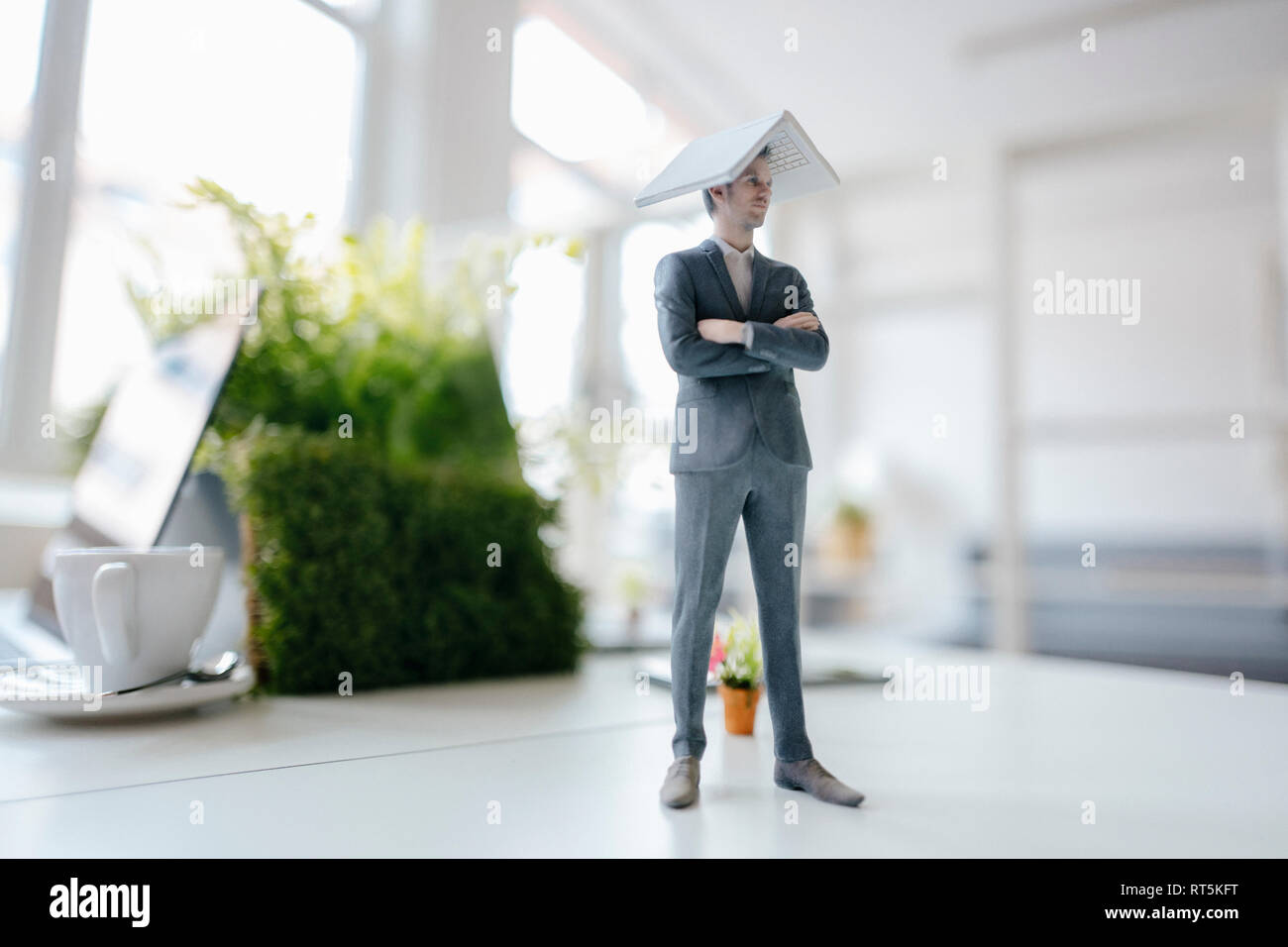Imprenditore figurina in piedi sulla scrivania, il bilanciamento di un computer portatile in cima Della sua testa Foto Stock