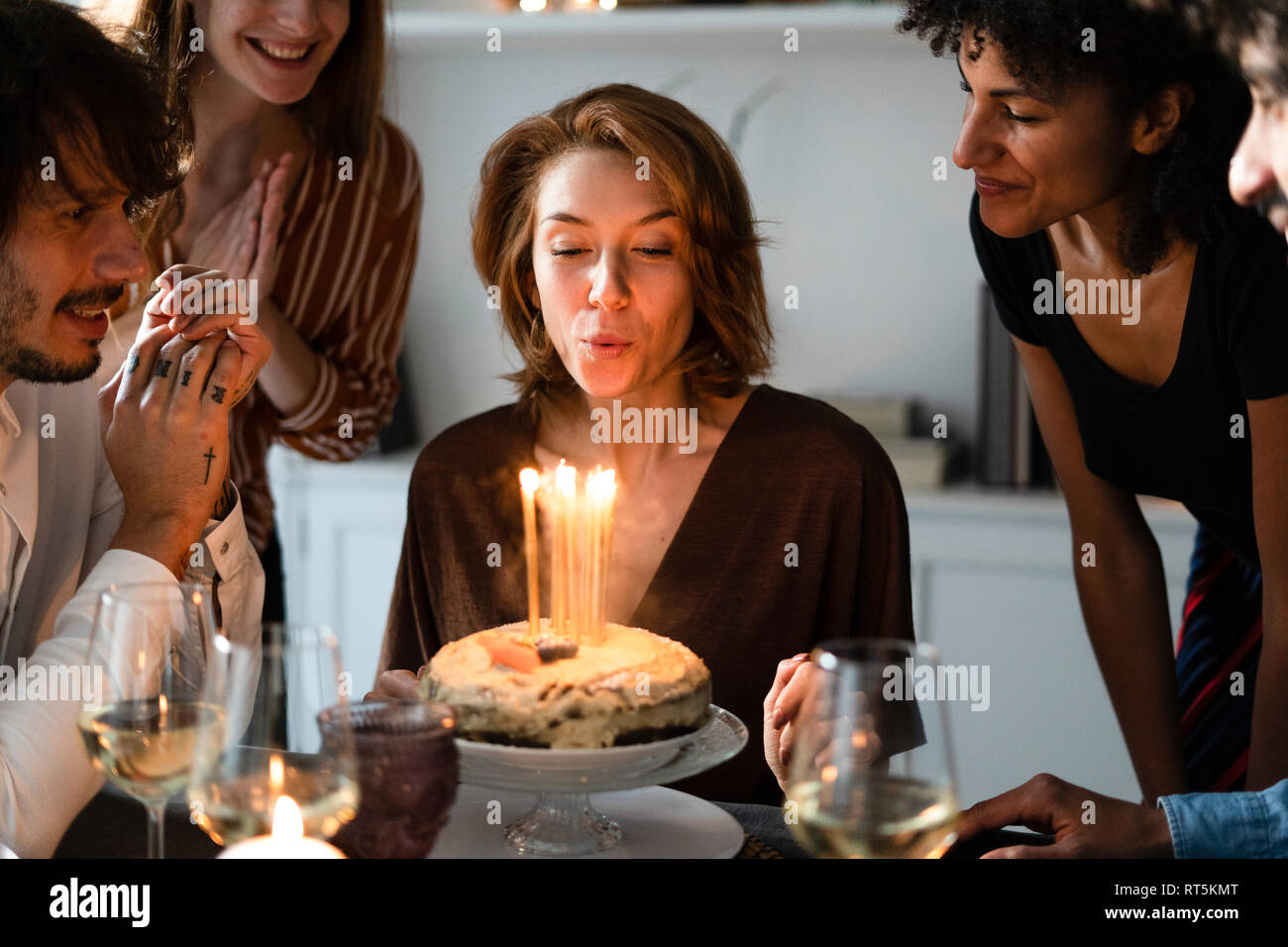 Amici celbrating compleanno di una giovane donna, che spegne le candeline sulla torta del compleanno Foto Stock
