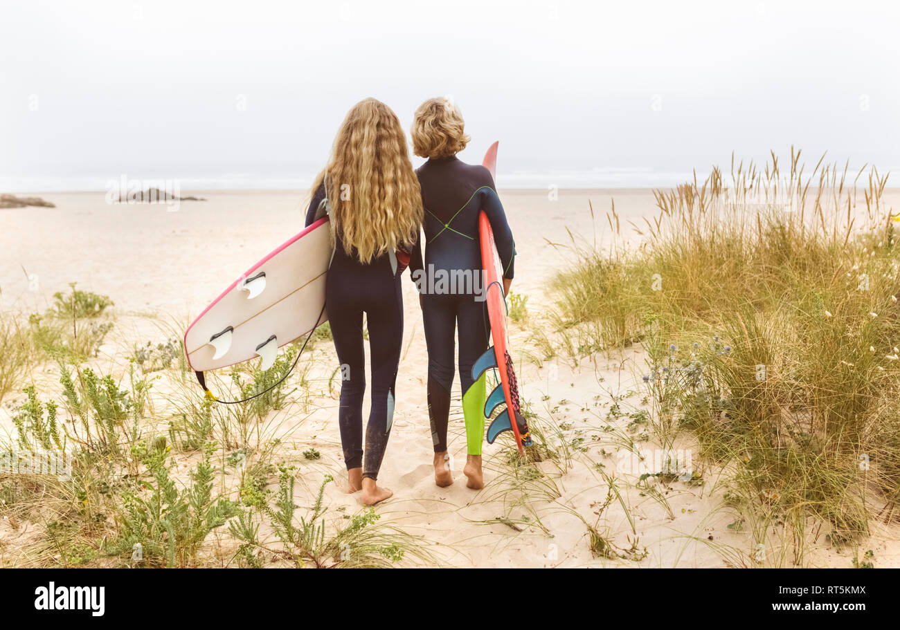 Spagna, Aviles, vista posteriore di due giovani surfisti sulla spiaggia Foto Stock