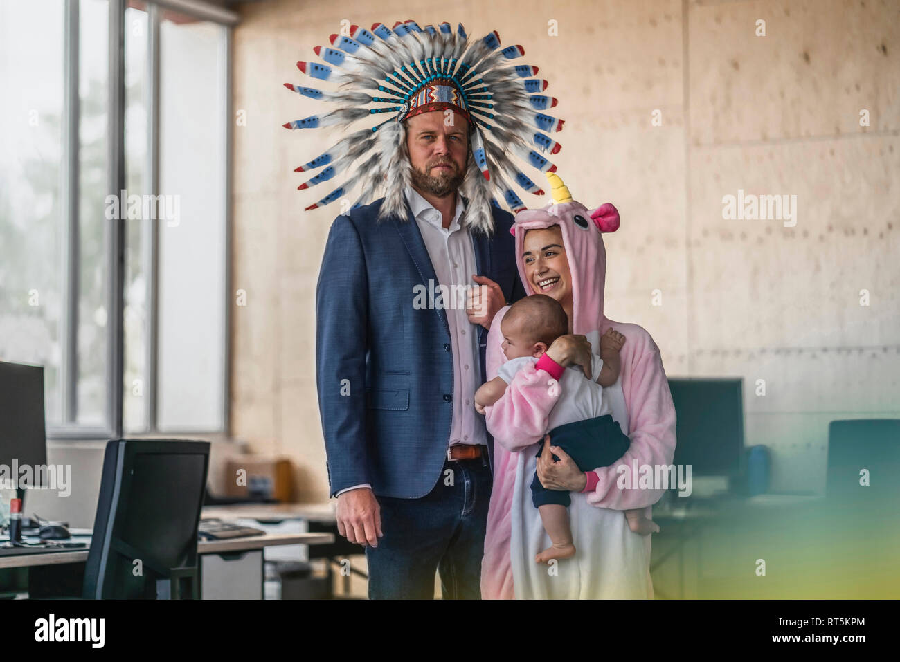 L uomo e la donna vestita come Indiani e unicorn, stando in ufficio, donna tenendo il bambino nelle braccia Foto Stock
