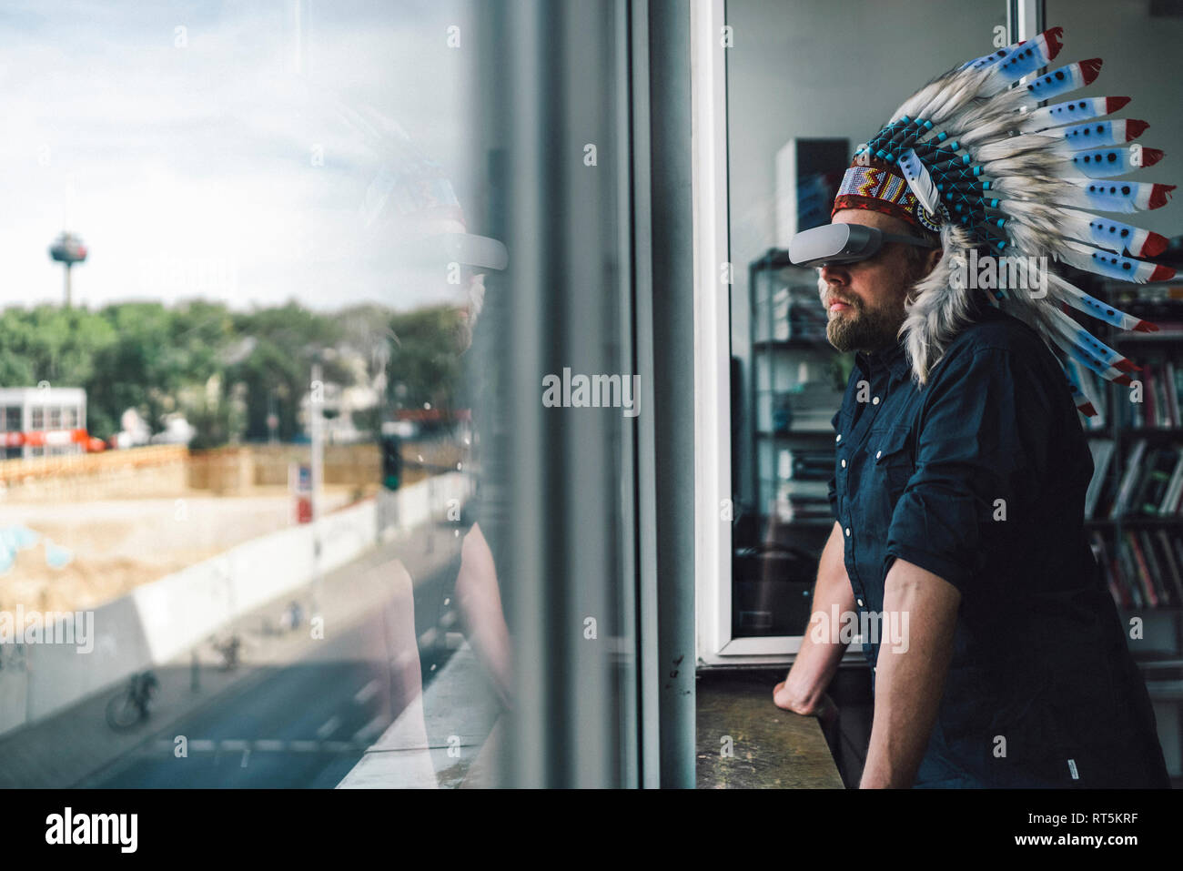 Uomo di indossare copricapo indiano e occhiali VR in ufficio, guardando fuori della finestra Foto Stock