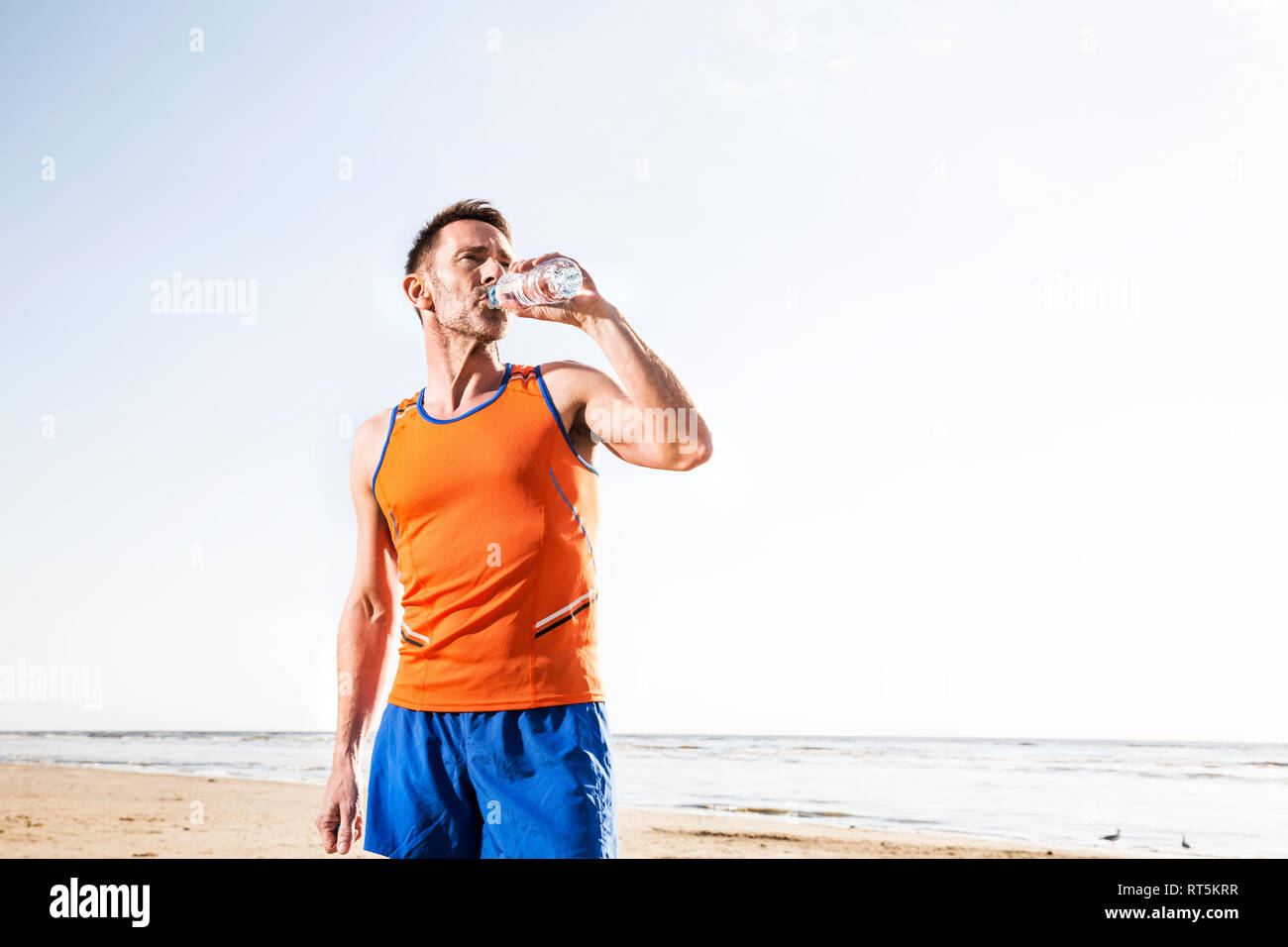 Atleta di bere dalla bottiglia sulla spiaggia Foto Stock