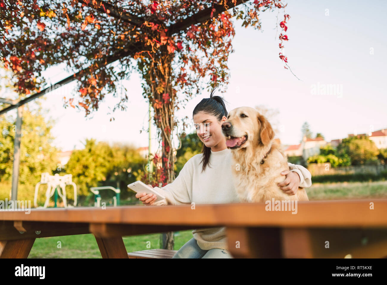 Sorridente ragazza con un telefono cellulare e il suo golden retriever cane di riposo in un parco Foto Stock