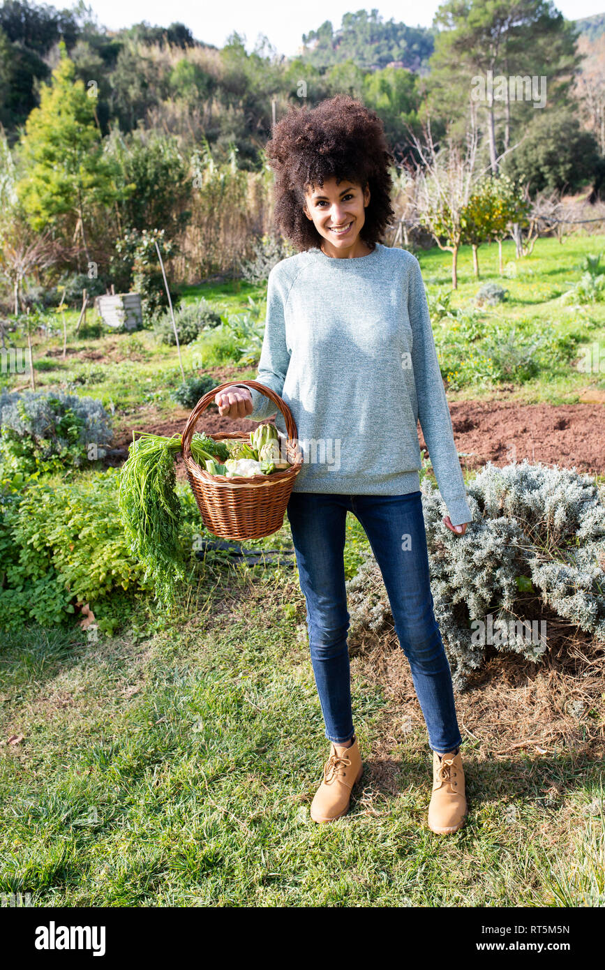 Donna in piedi nel campo, portando una cassa di ortaggi Foto Stock