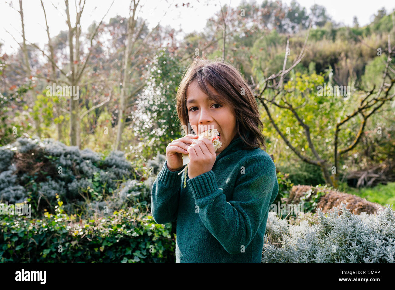 Ragazzo in piedi in giardino, prendendo una pausa, mangiando panini Foto Stock