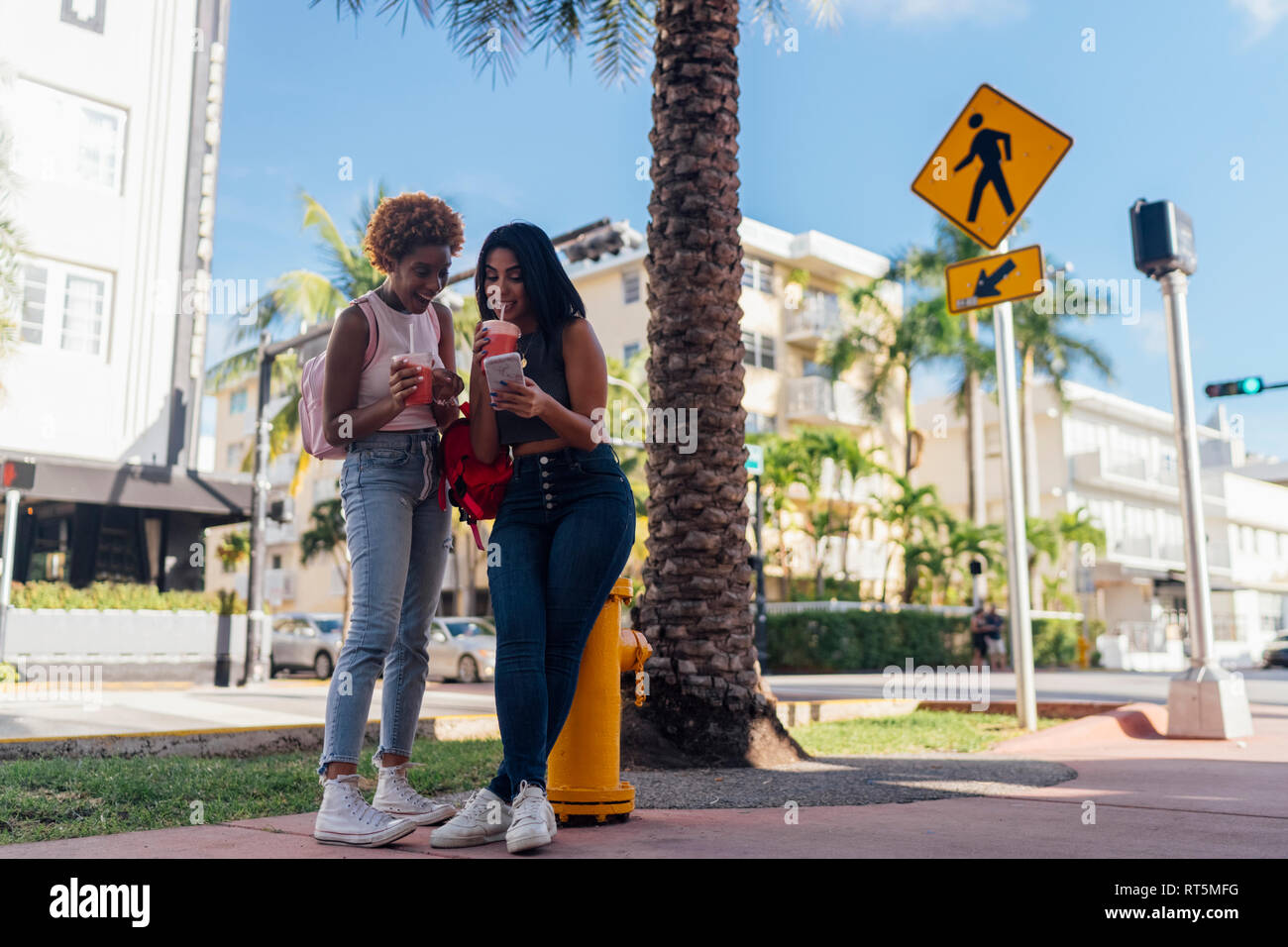 Stati Uniti d'America, Florida, Miami Beach, due happy amici di sesso femminile con un telefono cellulare e soft drink in città Foto Stock