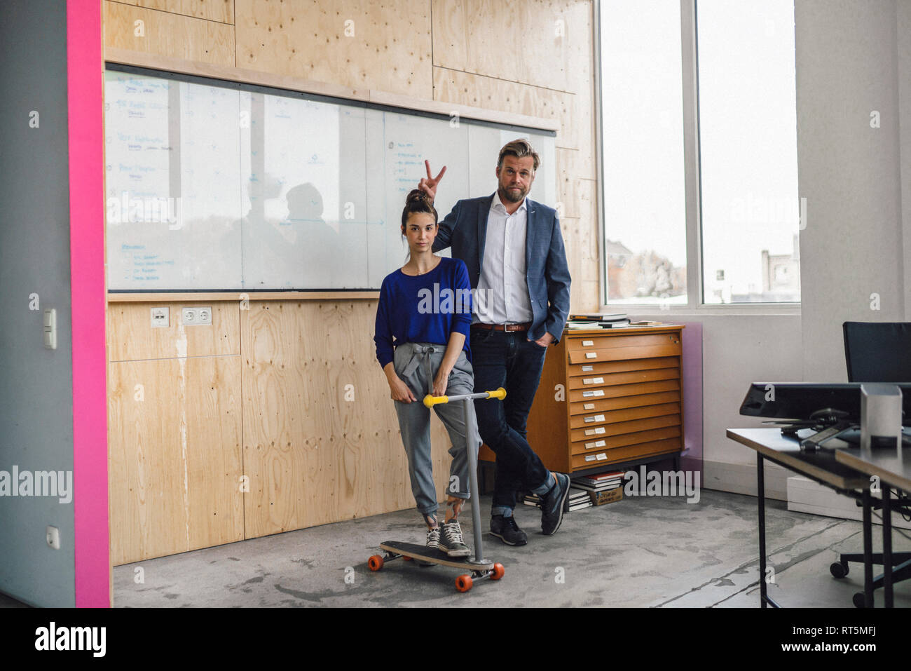 Uomo maturo e il suo assistente a giocare con gli scooter, stando in ufficio nella parte anteriore del pannello bianco Foto Stock