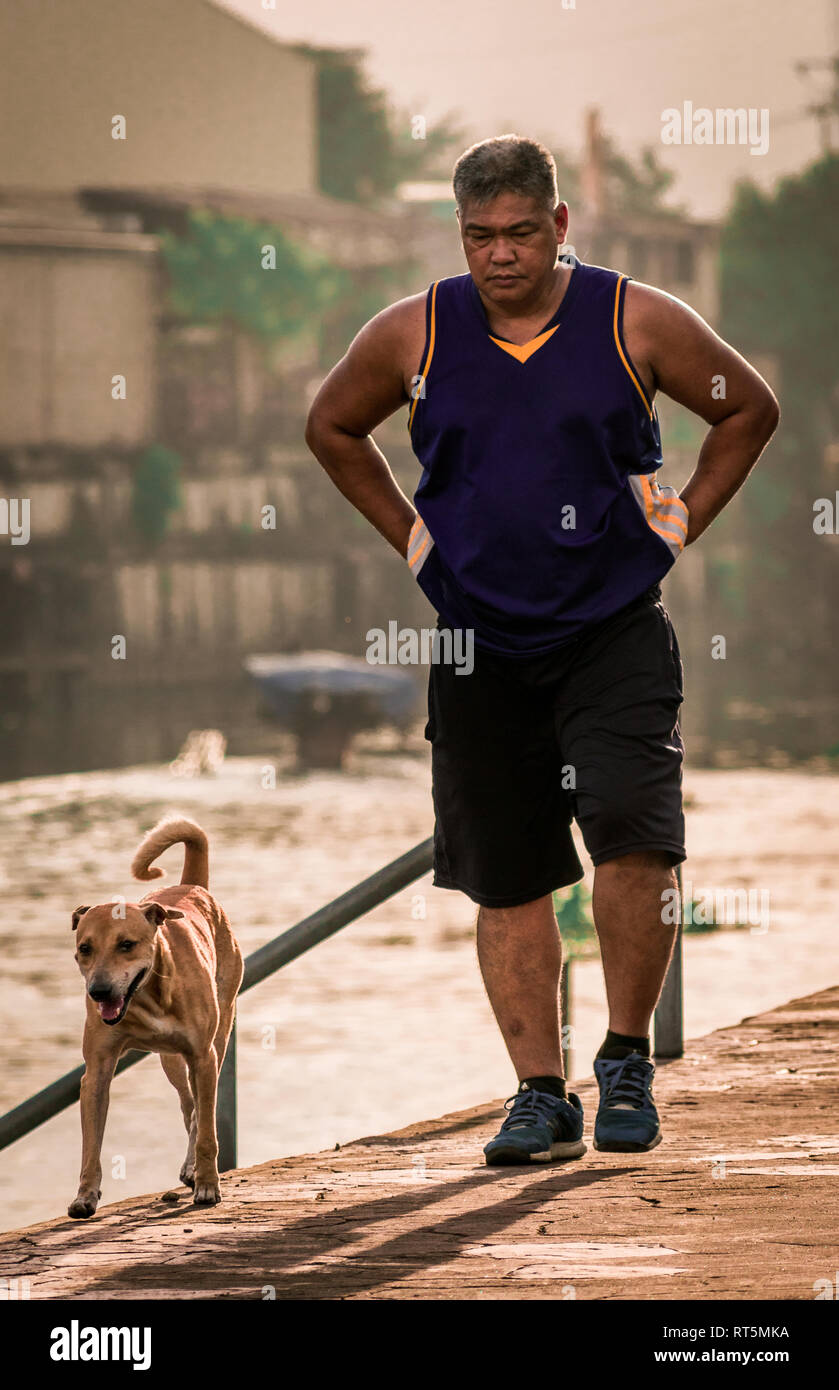 Uomo che cammina il suo cane mentre godendo il sole del mattino accanto al fiume. Foto Stock